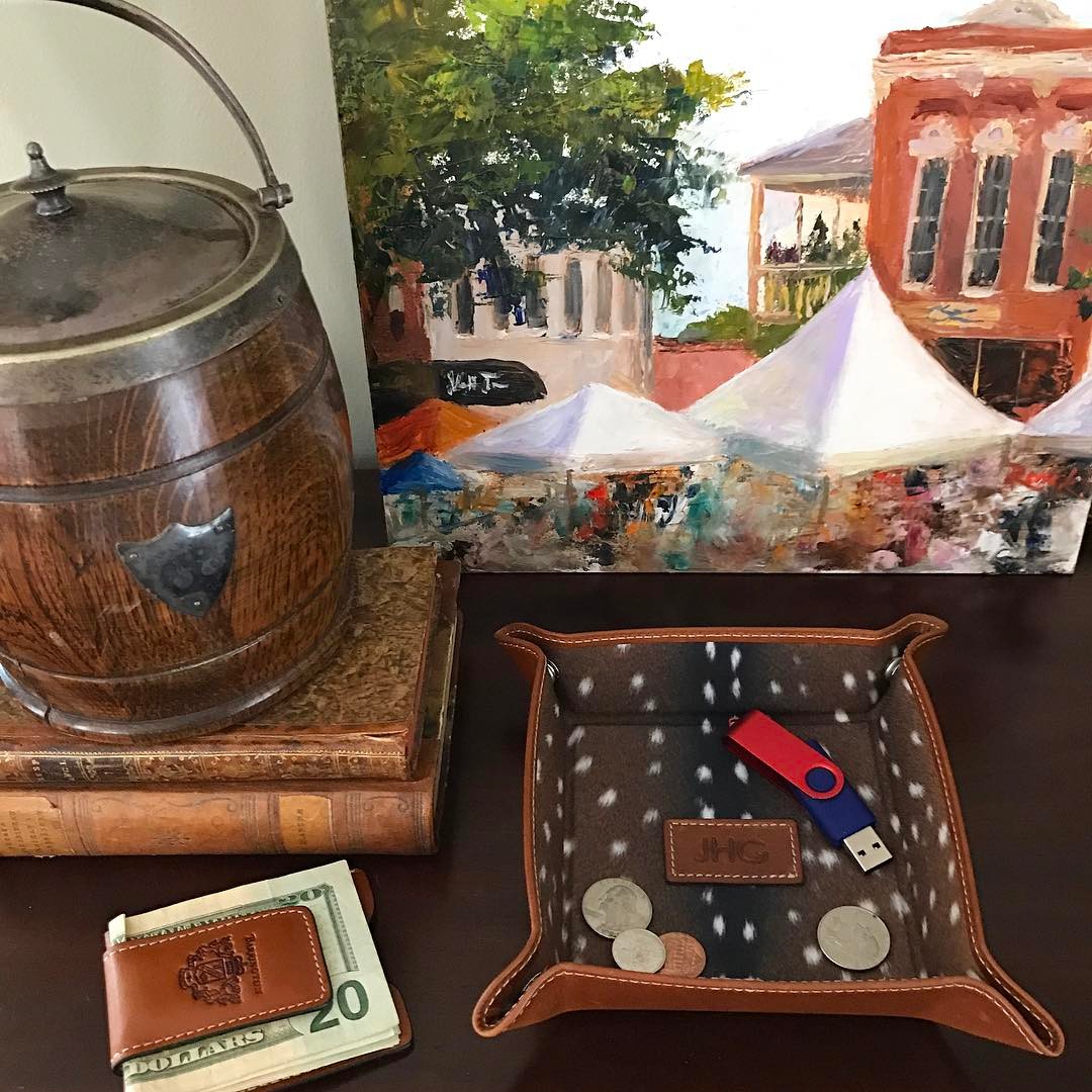 A finely crafted British tan leather money clip, holding currency, showcased alongside a leather valet tray and antique items, highlighting its timeless design, quality, and superior craftsmanship.
