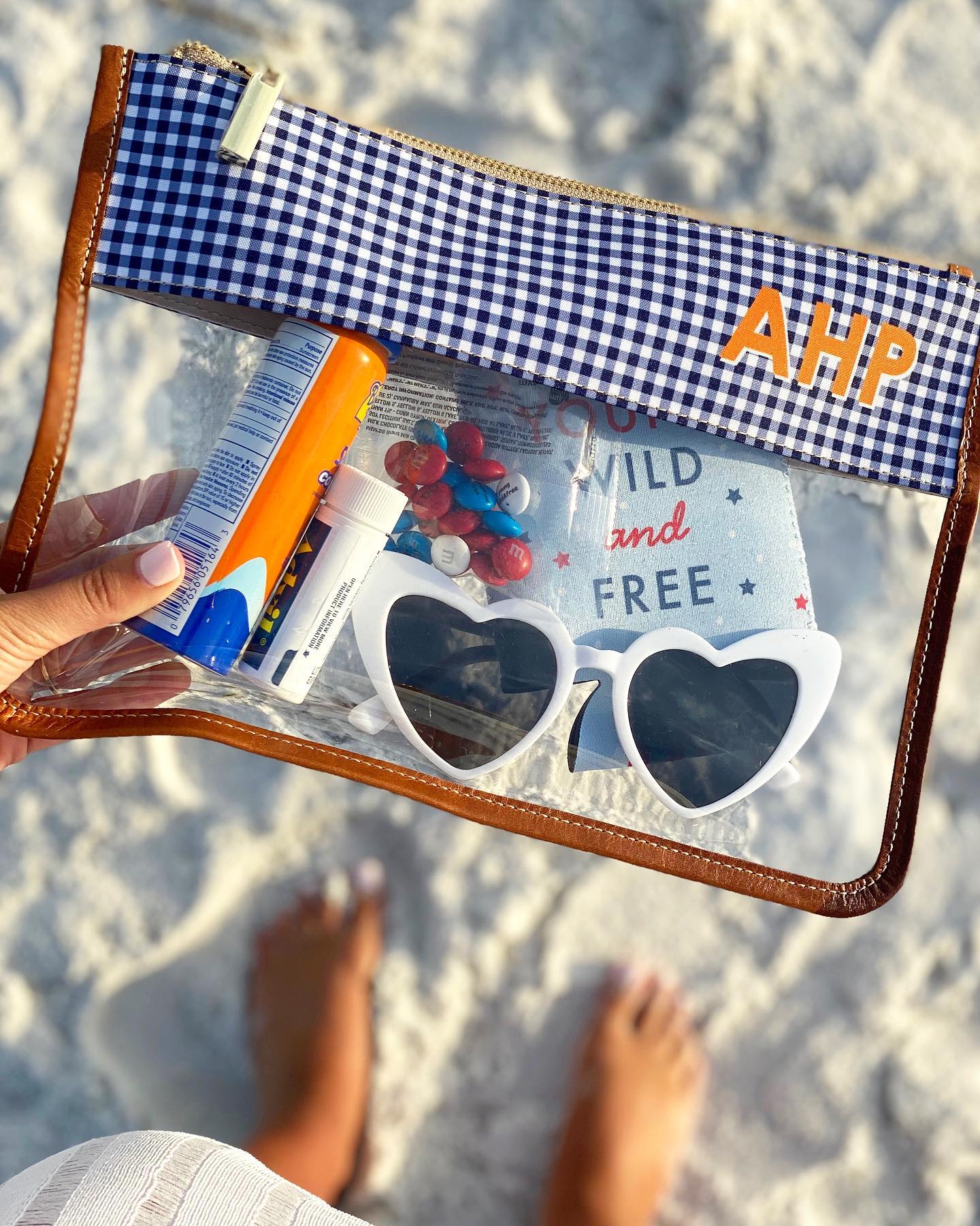 A monogrammed clear pouch with beach essentials, initialed AHP, on a sandy beach